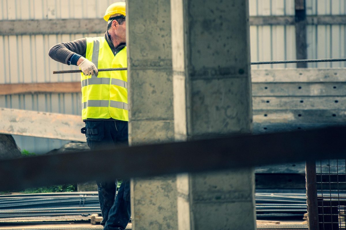 Construction worker in a high-visibility vest carrying reinforcement steel on site